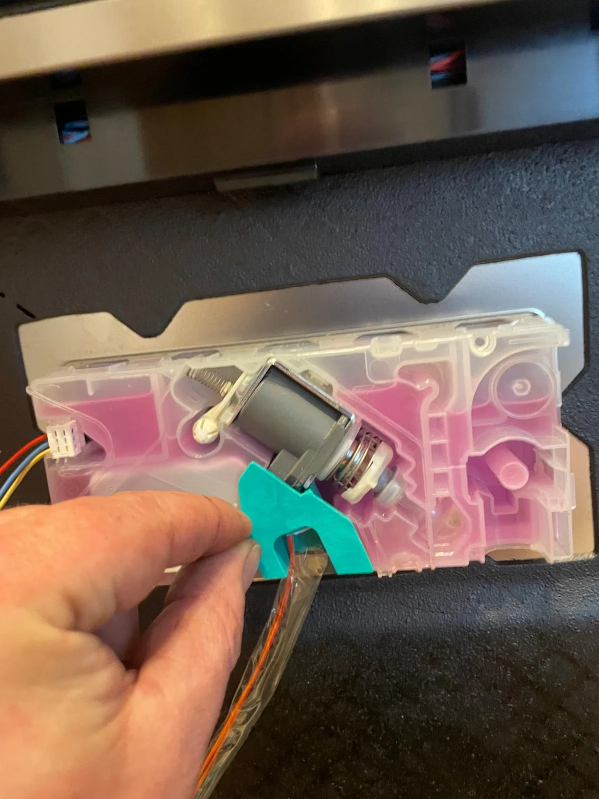 A brand new replacement dishwasher detergent dispenser unit being prepared for installation to fix a noisy clicking fault.